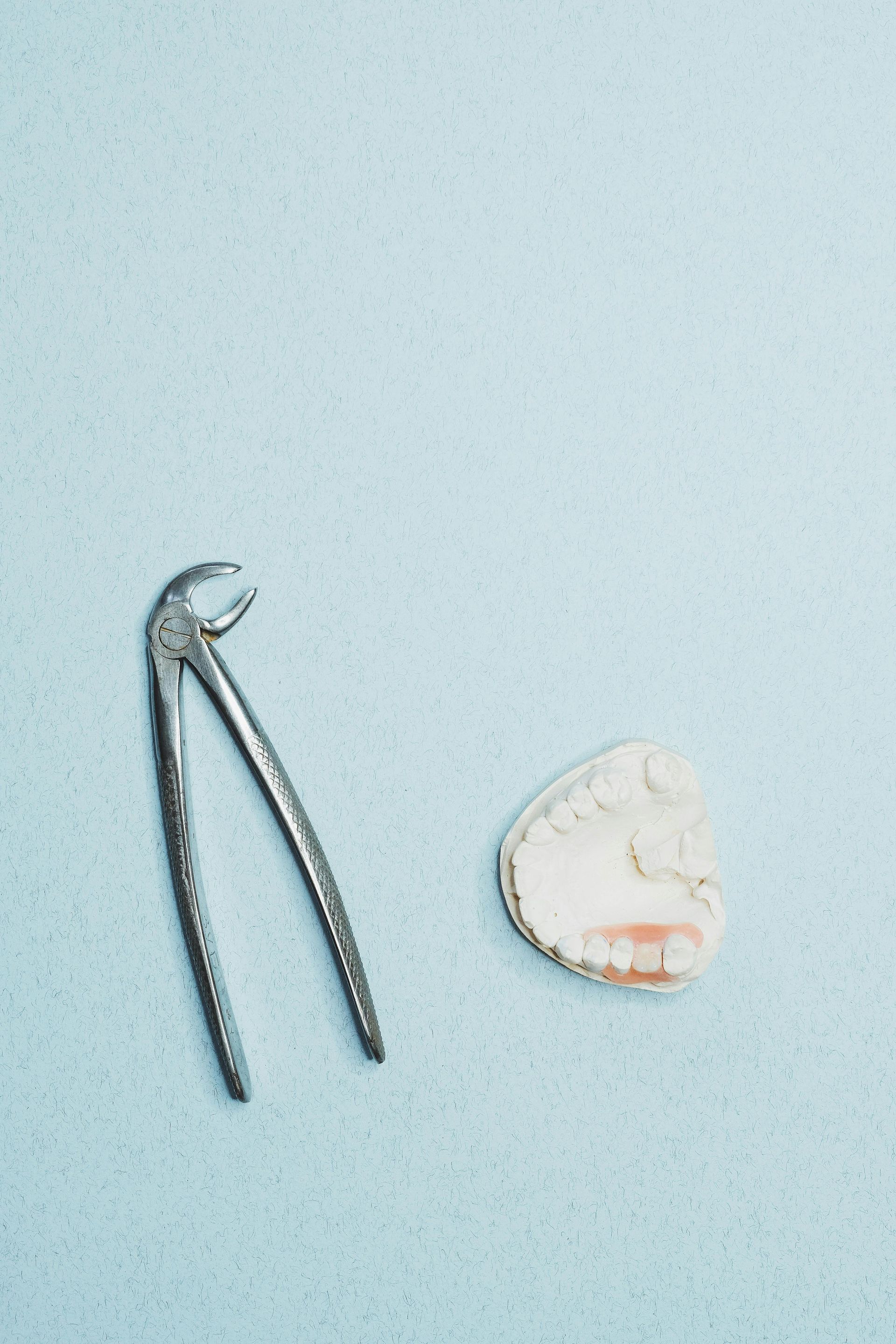 Dental extraction tools and a tooth mold on a light blue surface.