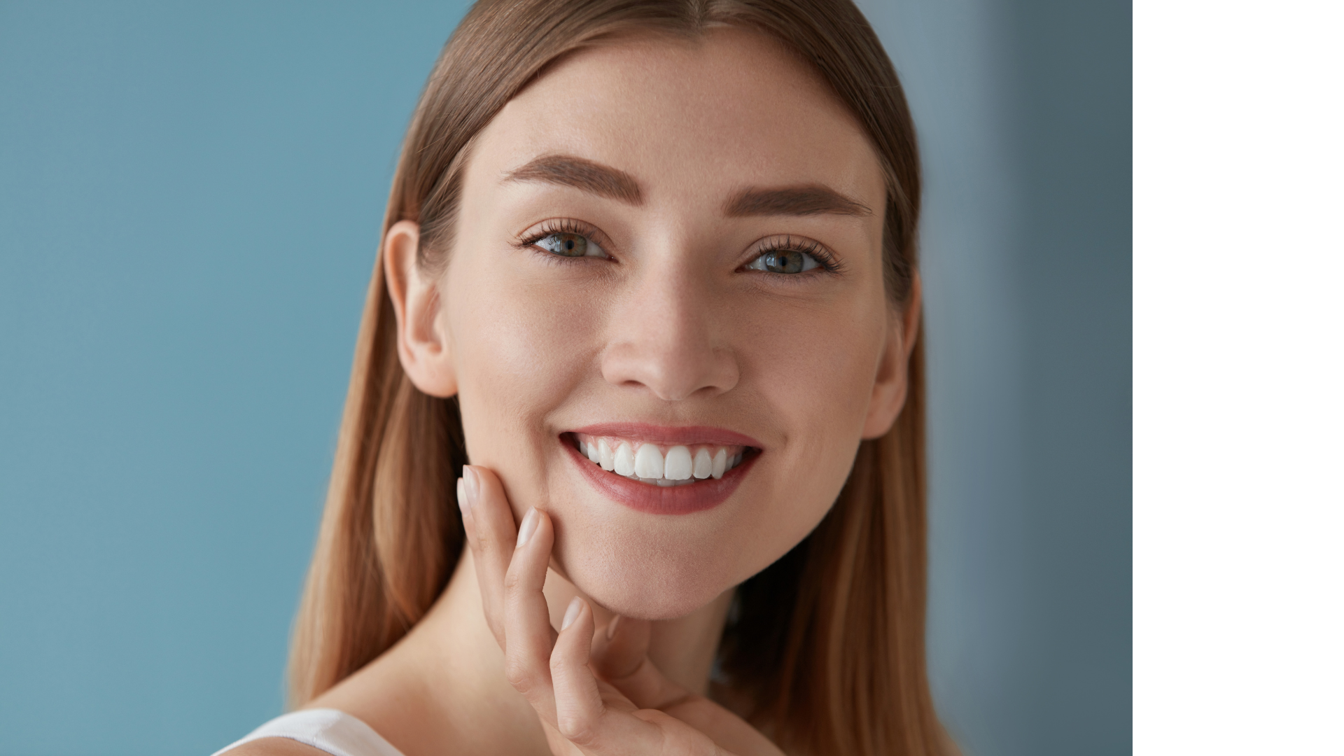 Woman smiling, touching her cheek, against a blue background.