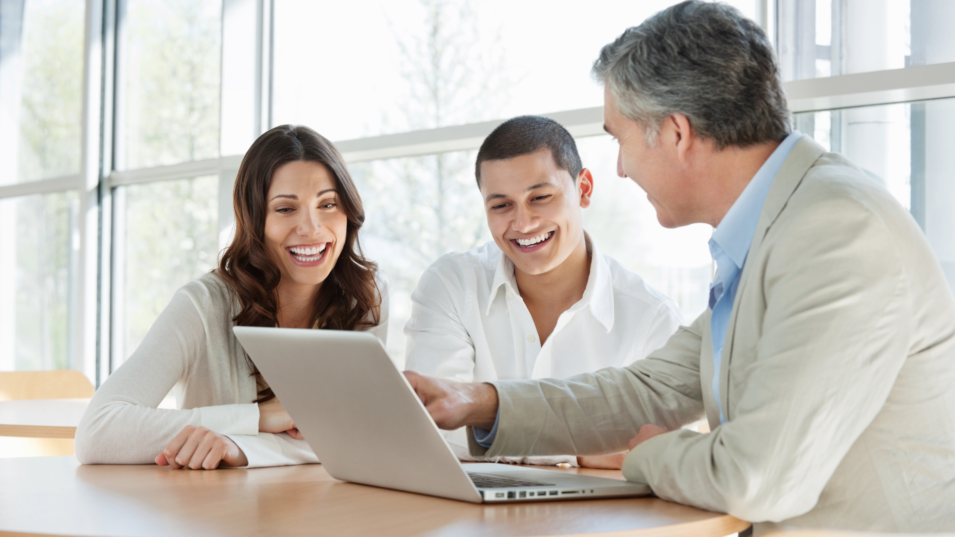 A man and a woman are sitting at a table looking at a laptop.