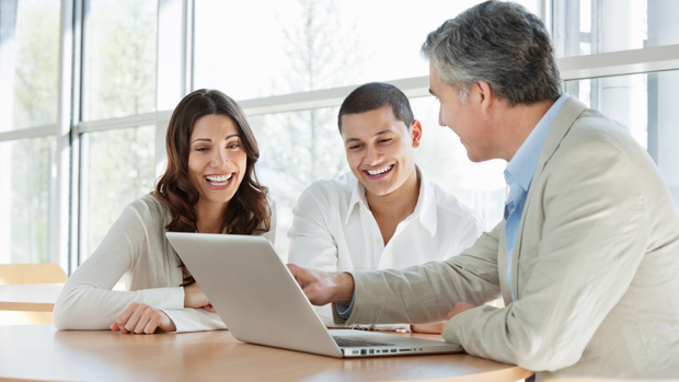 A man and a woman are sitting at a table looking at a laptop.