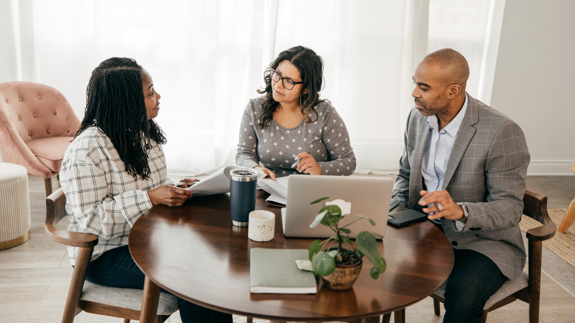 A group of people are sitting around a table with laptops.