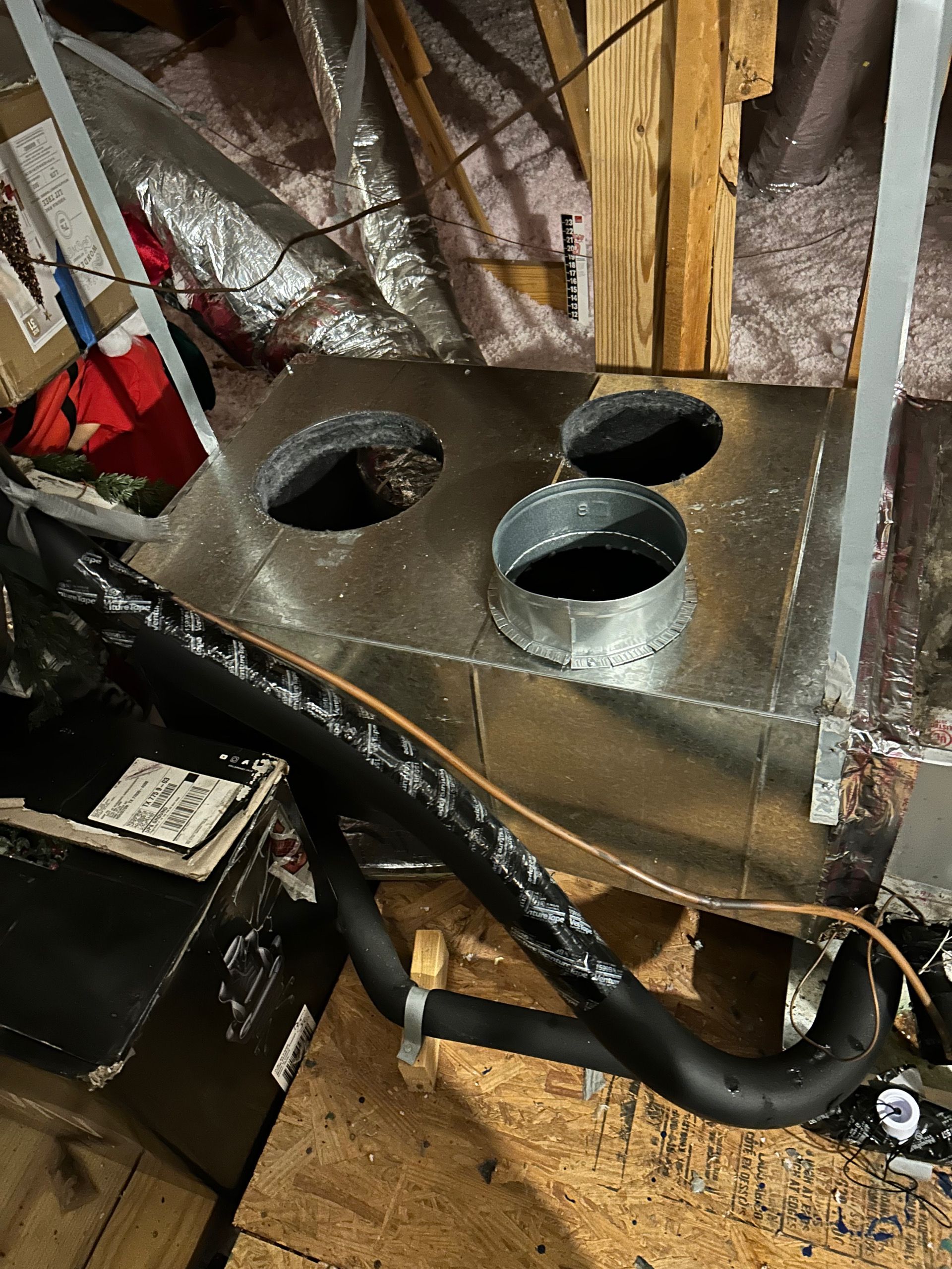 HVAC ductwork with three round openings and insulated black refrigerant lines in an attic space.