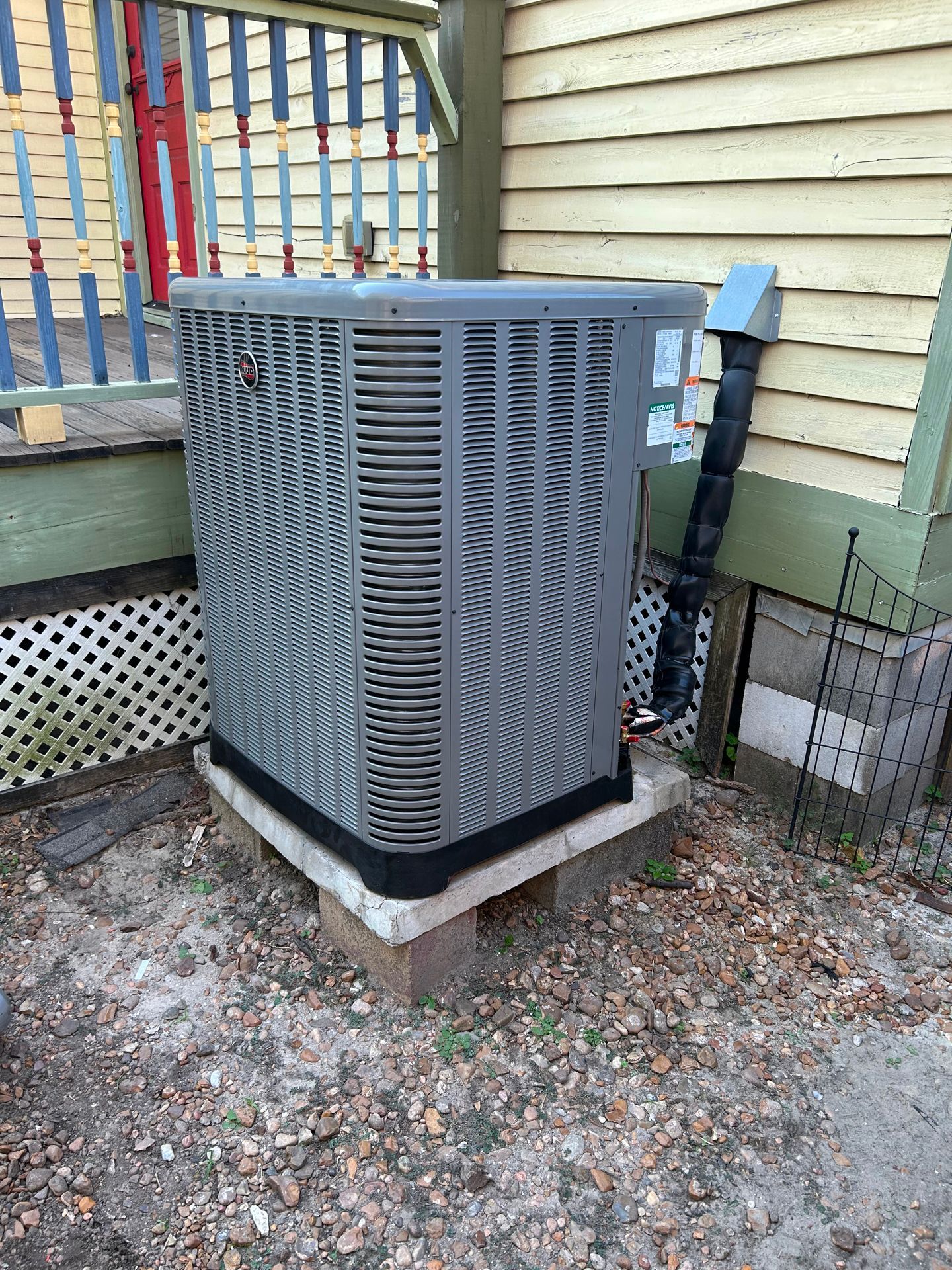 Central air conditioner unit on concrete blocks next to a wall and decorative fence.