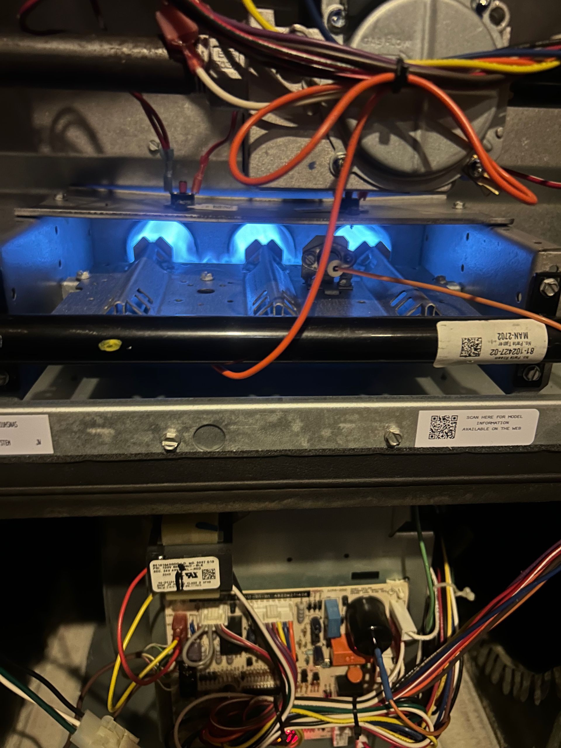 Furnace interior with blue flames from burners, wires and control panel visible.