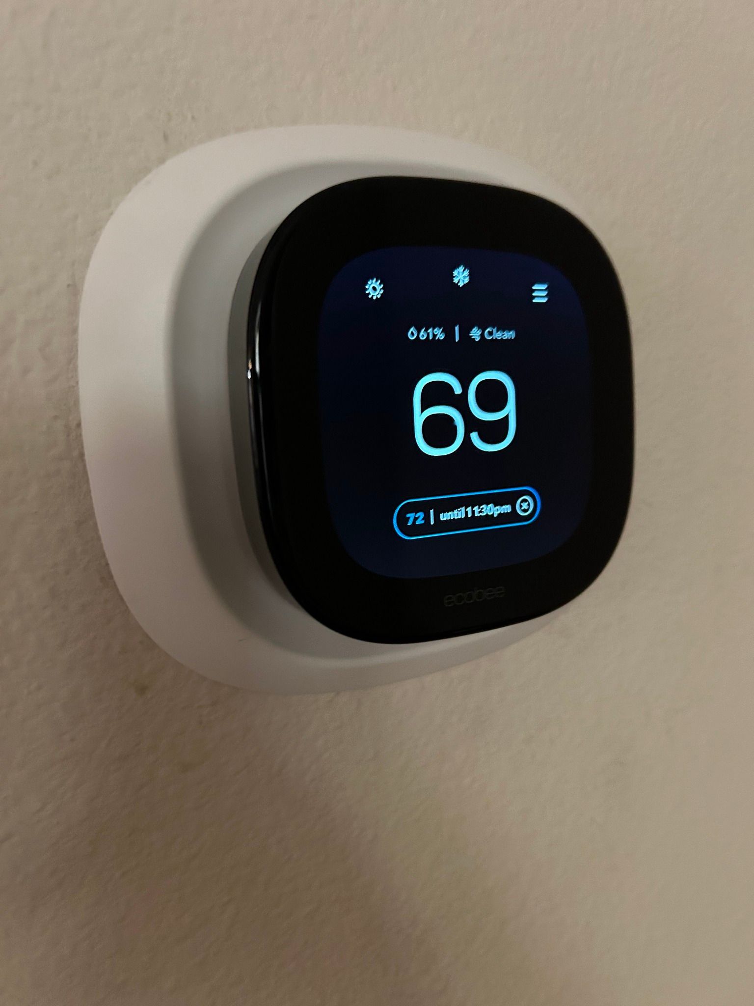 A smart thermostat displays 69 degrees. It is mounted on a white wall.
