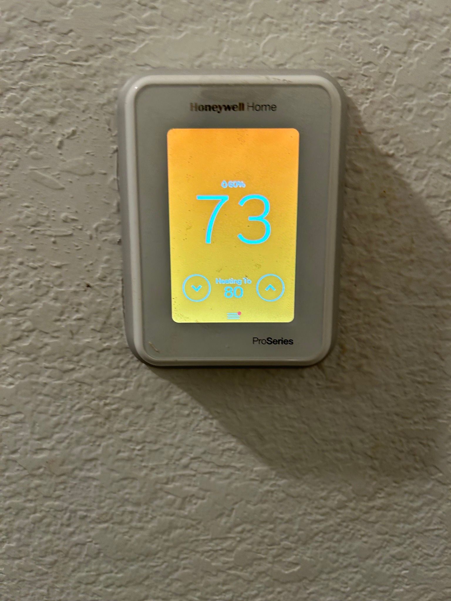 Honeywell thermostat displays 73 degrees. Gray frame on textured wall.