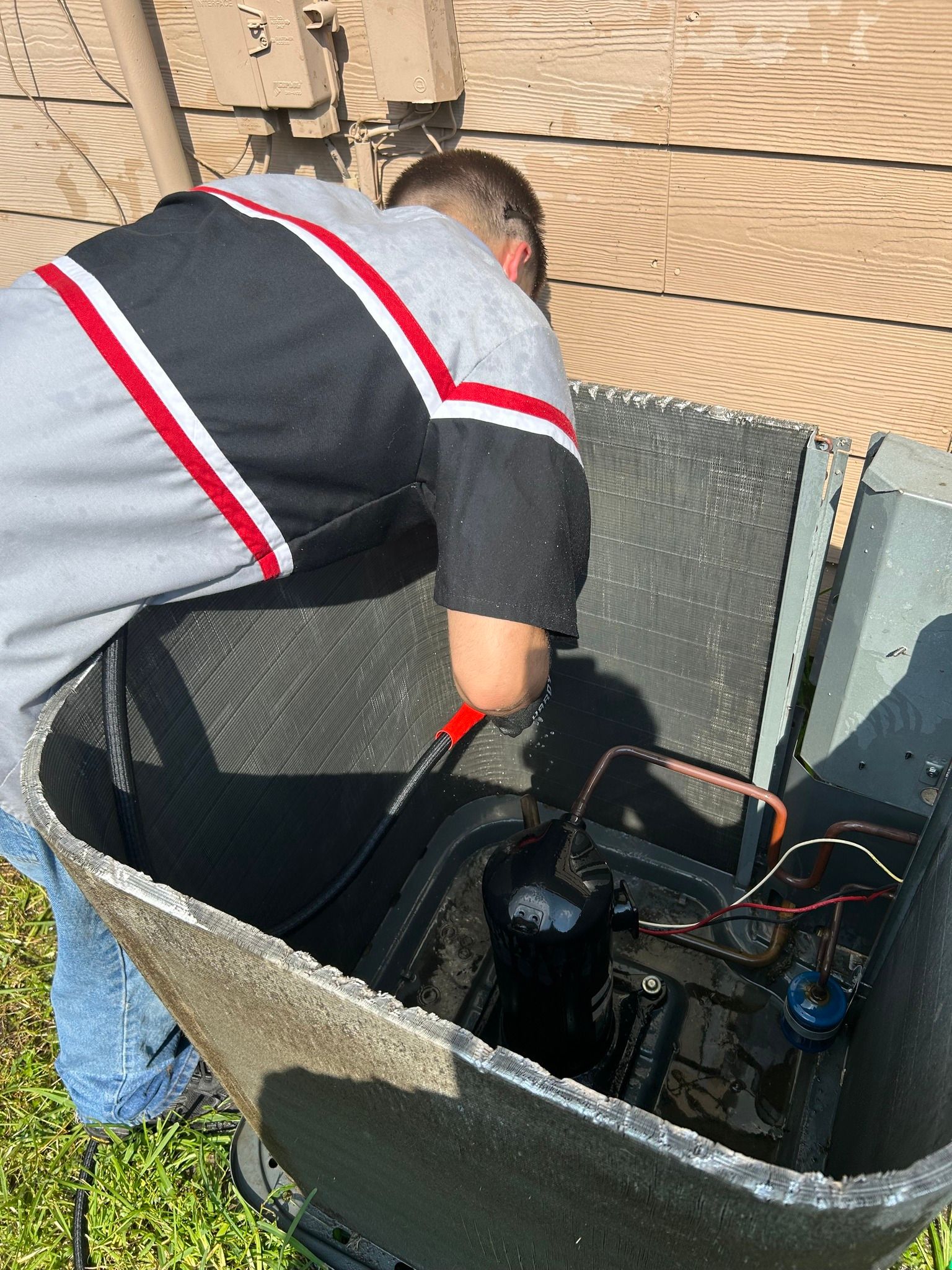Person cleaning an air conditioning unit outside, using a hose.