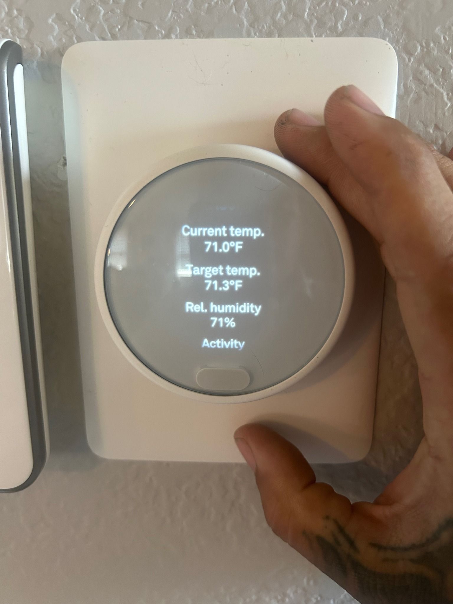 Hand adjusting a white smart thermostat displaying current temperature, target temperature, and humidity levels.