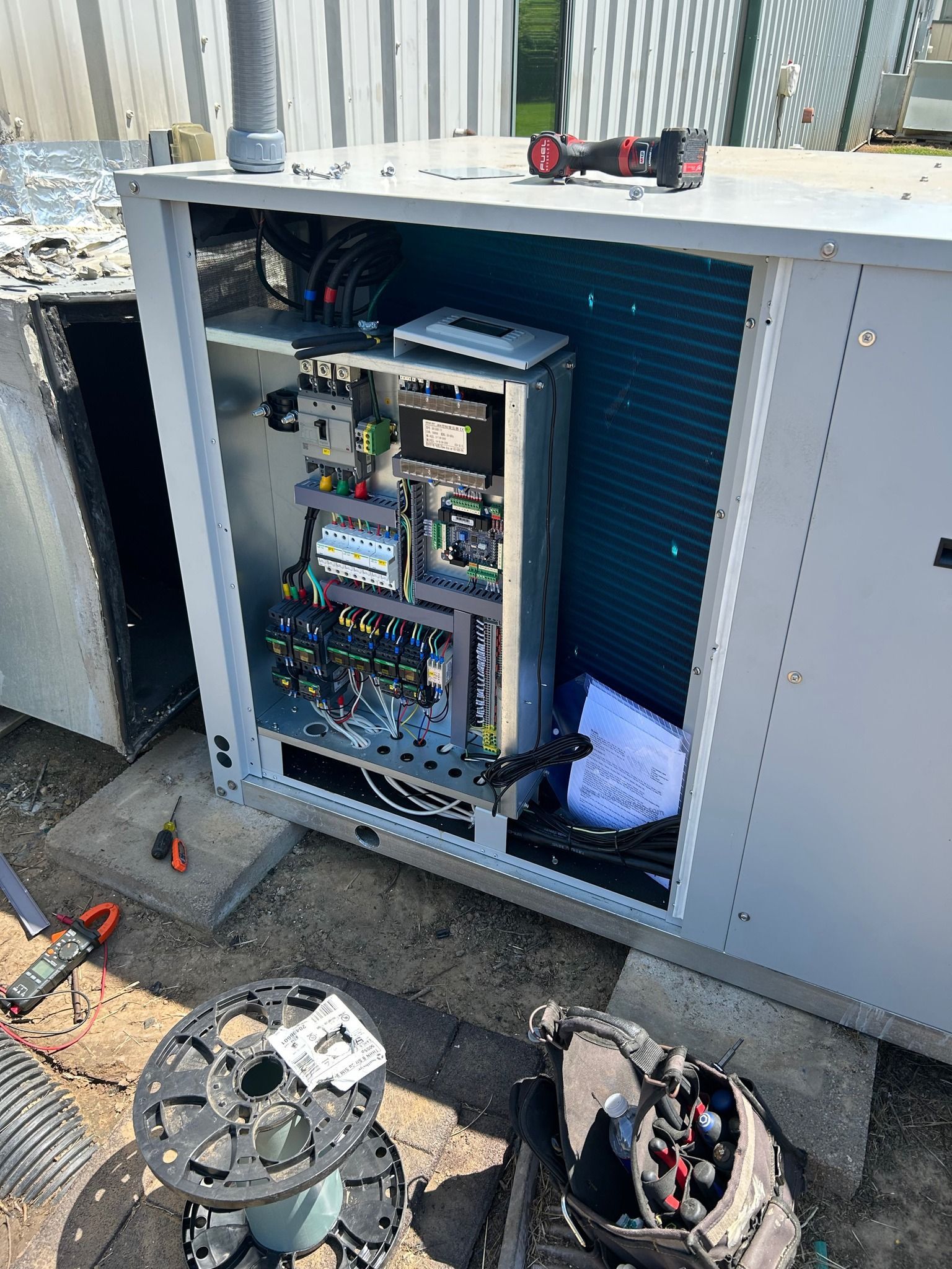 HVAC unit with open panel, showing electrical components. Tools and parts are scattered around a rooftop.
