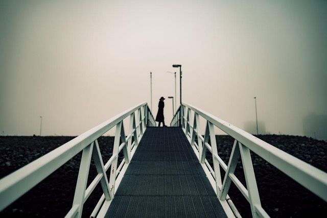 Een persoon die op een brug staat met een witte leuning