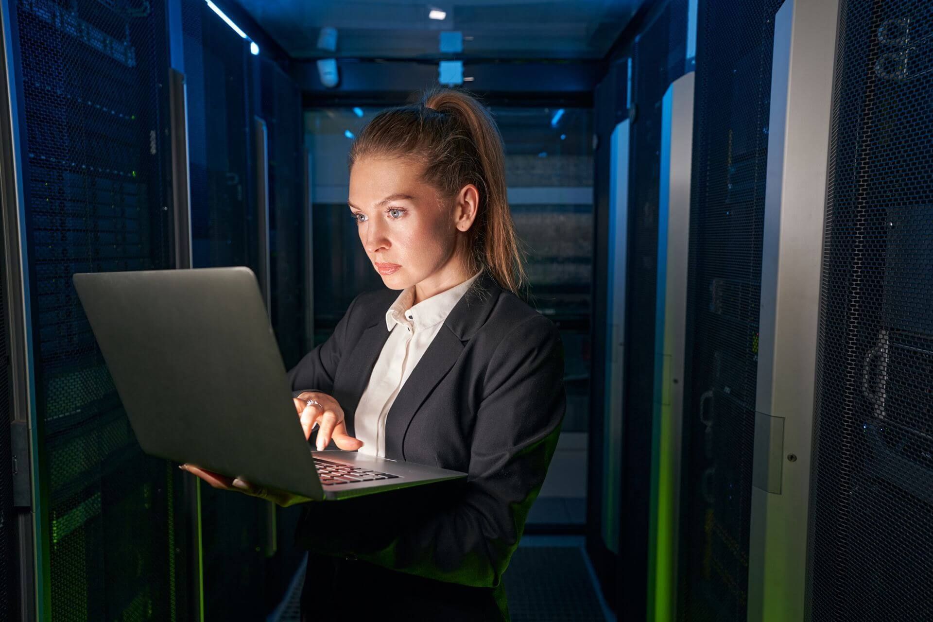 a woman is working on a laptop in a server room