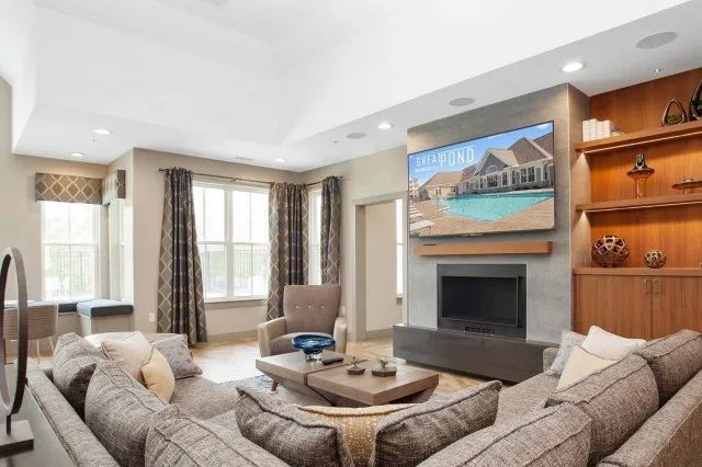 The Residences at Great Pond apartment with fire place, TV, sofa, and windows. 