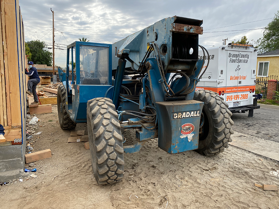 A blue forklift is parked on the side of the road next to a white van.