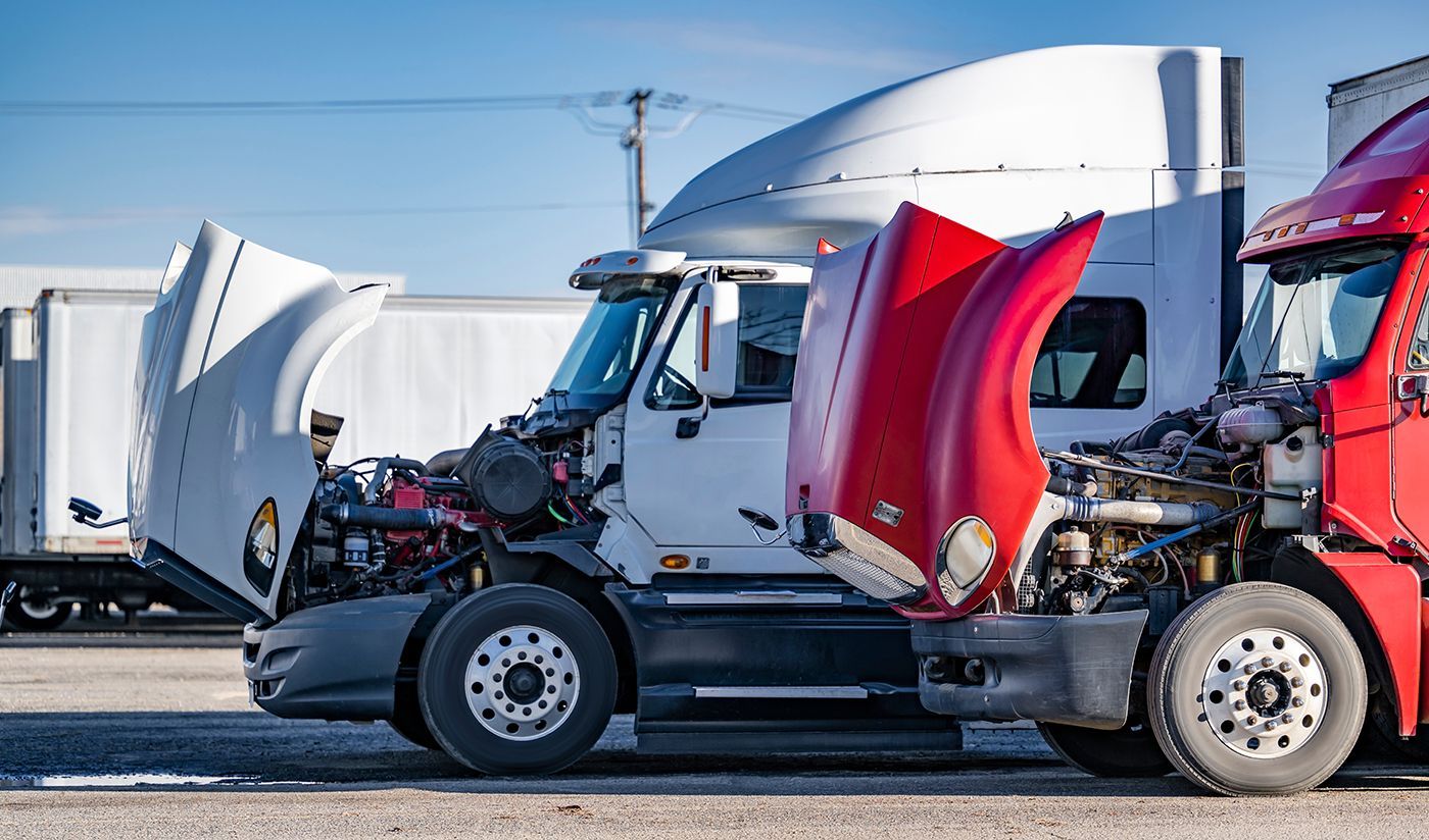 Two semi-trucks, white and red, with open hoods, parked outside.