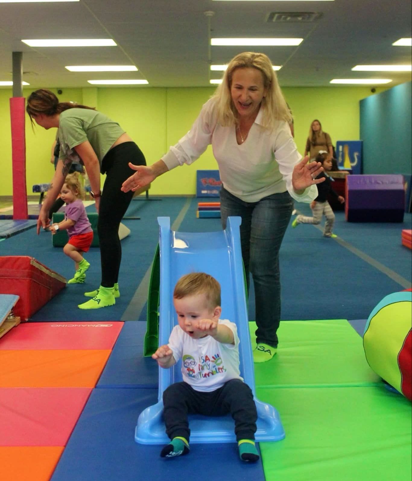 A woman playing with a baby on a slide in a gym