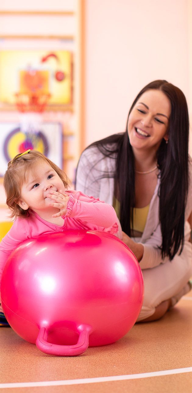A woman and a little girl are playing with a pink ball.
