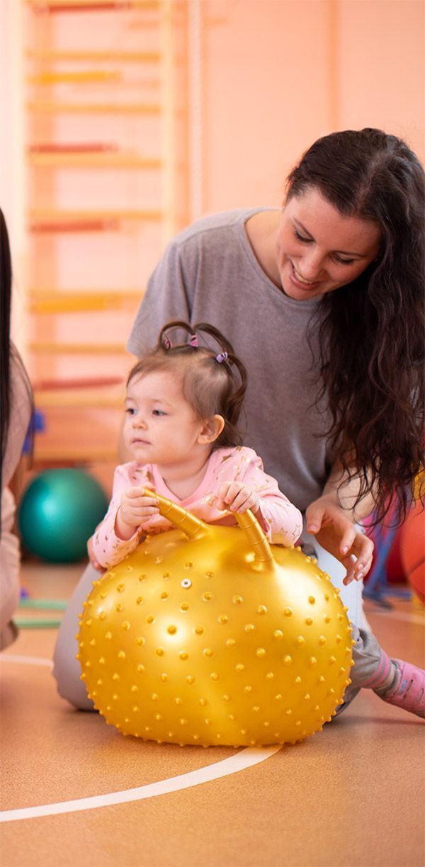 A woman is playing with a baby on a yellow exercise ball.