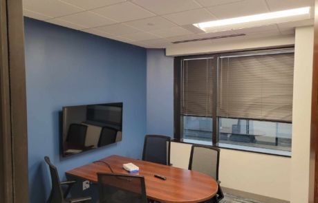 A conference room with a table and chairs and a flat screen tv on the wall.