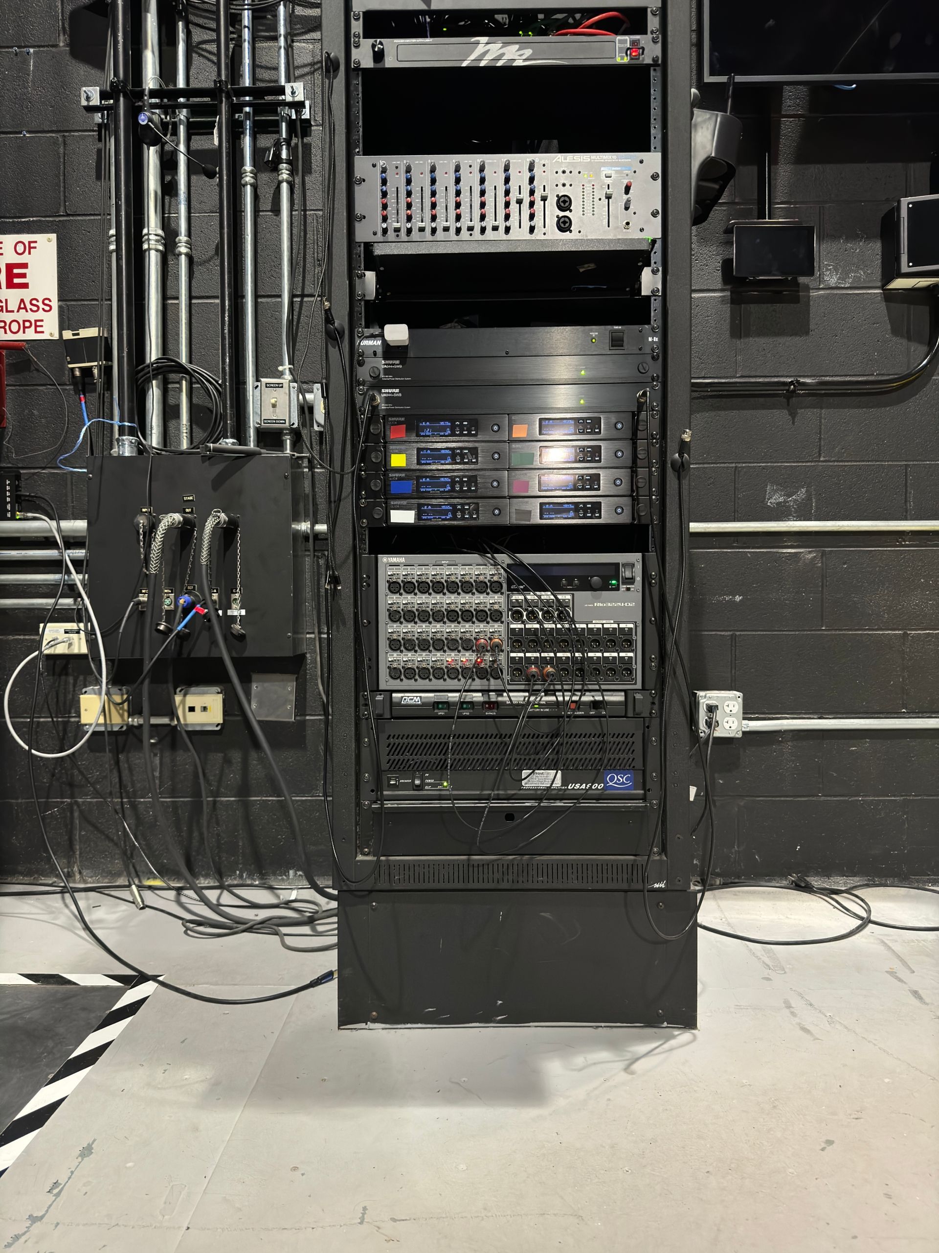A rack with a lot of electronics on it in a room with a fire exit sign