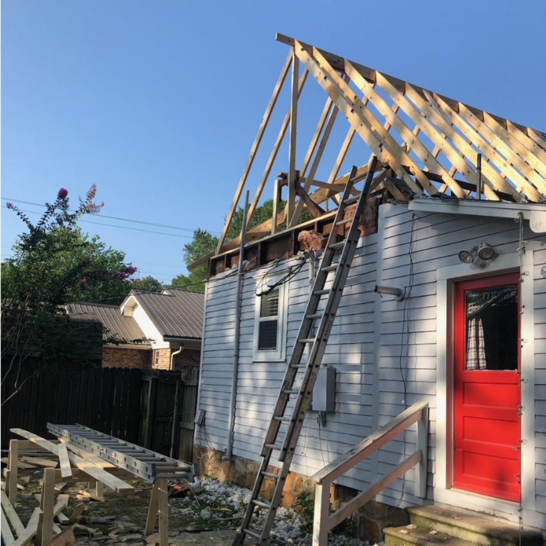 Exterior of house with roof damage from a fire, charred wood, white siding, blue sky.
