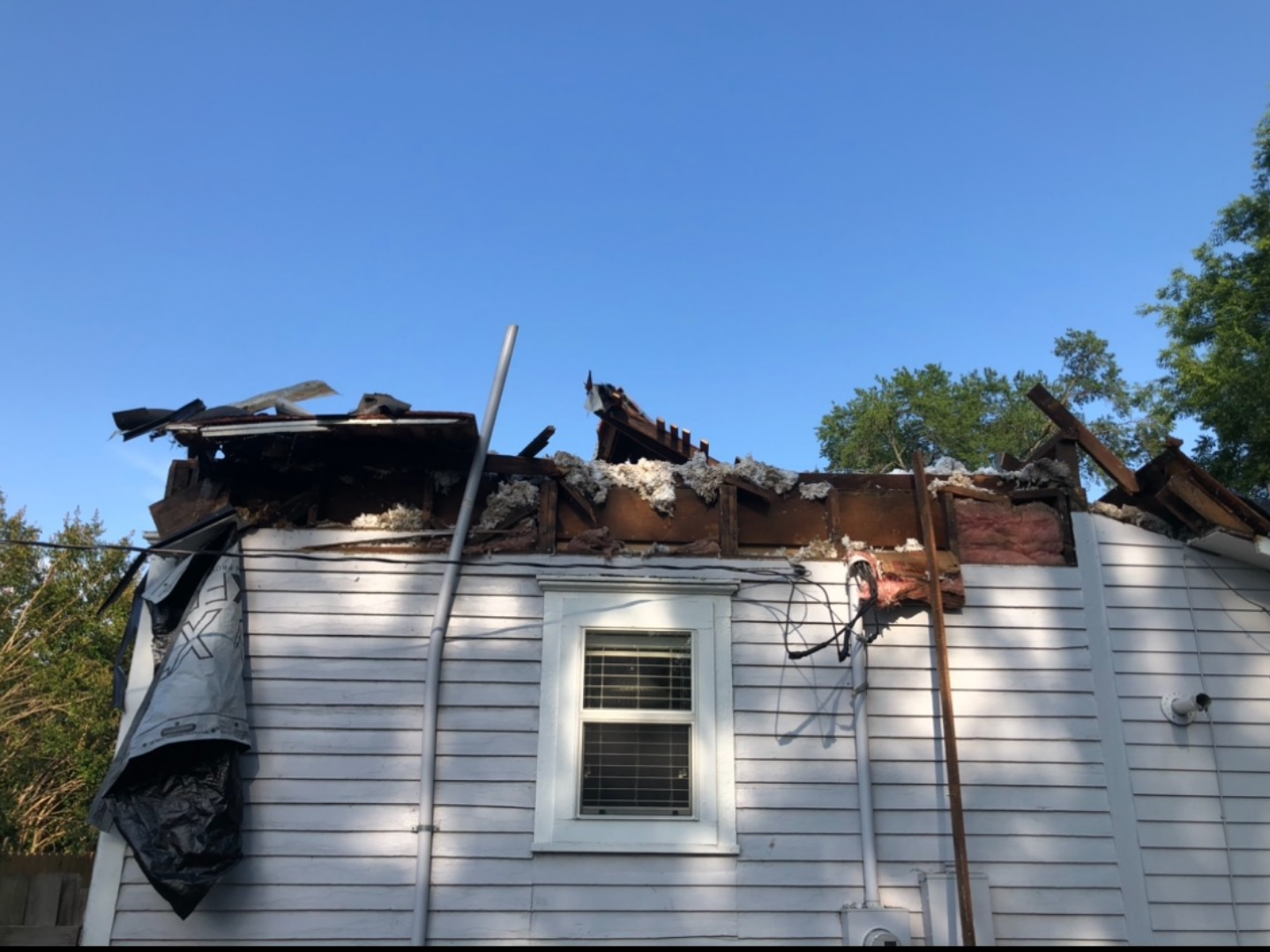House with a destroyed roof and a boarded-up window, damage from a fire.