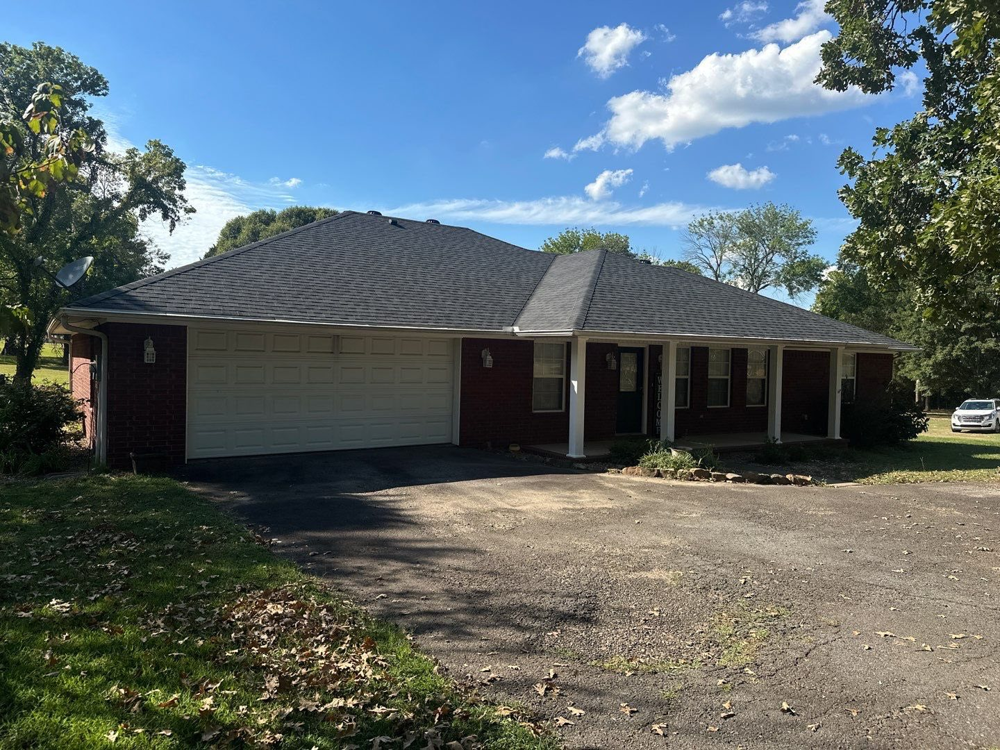 Red brick house with gray roof, white garage door, porch, and driveway on a sunny day.