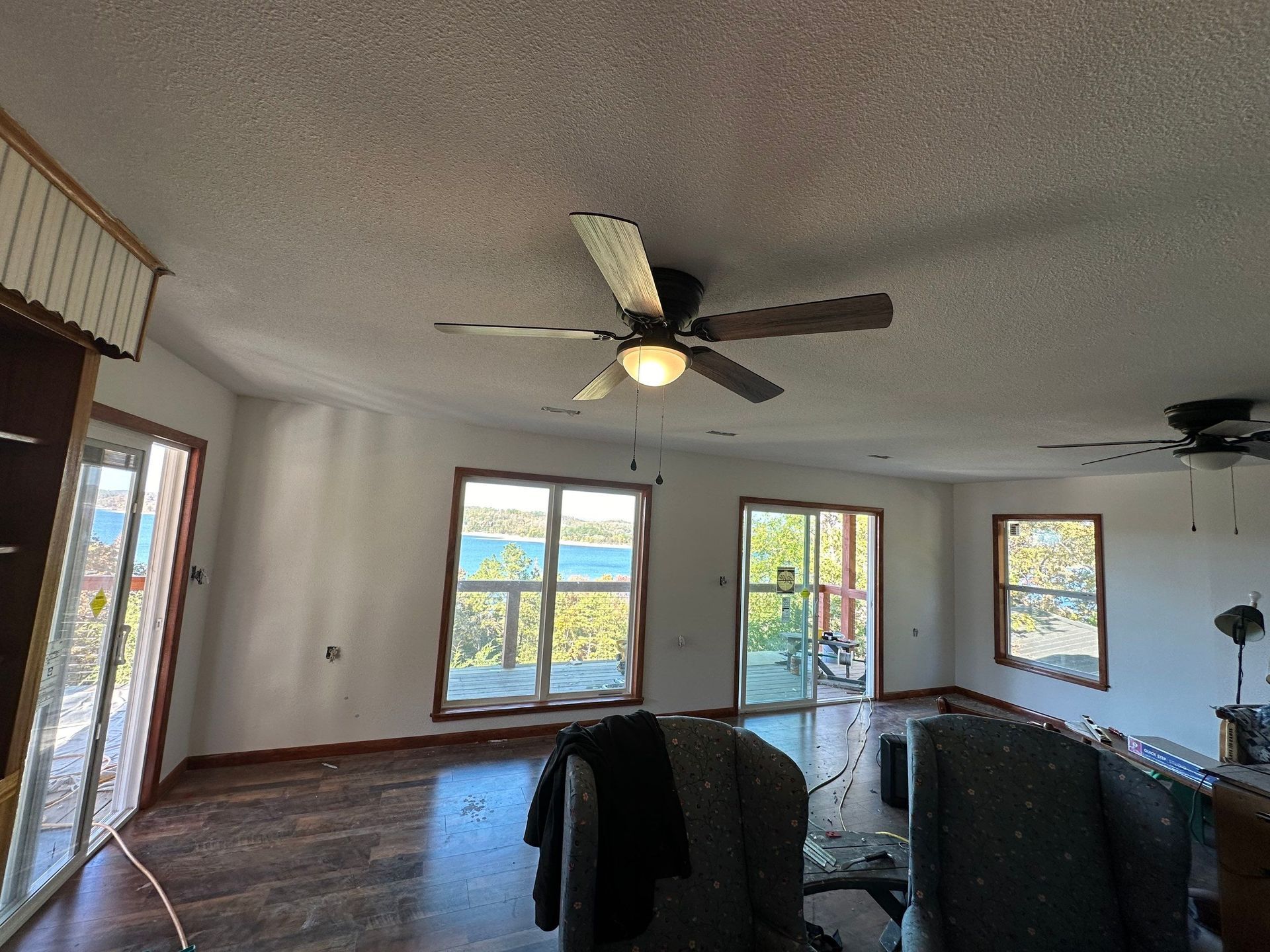 Living room with a ceiling fan and windows overlooking a lake.