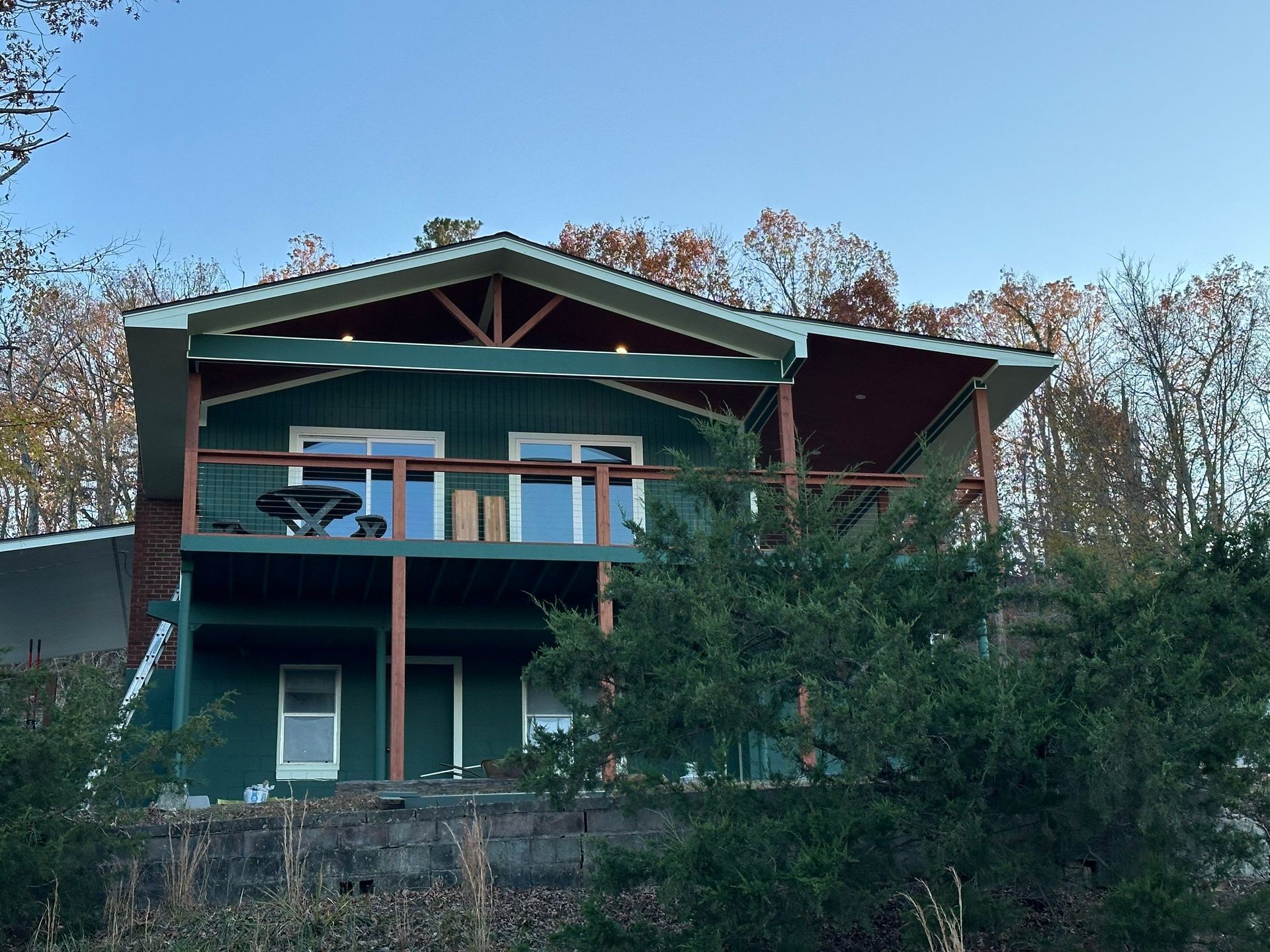 Green two-story house with deck; trees in the background, clear sky.