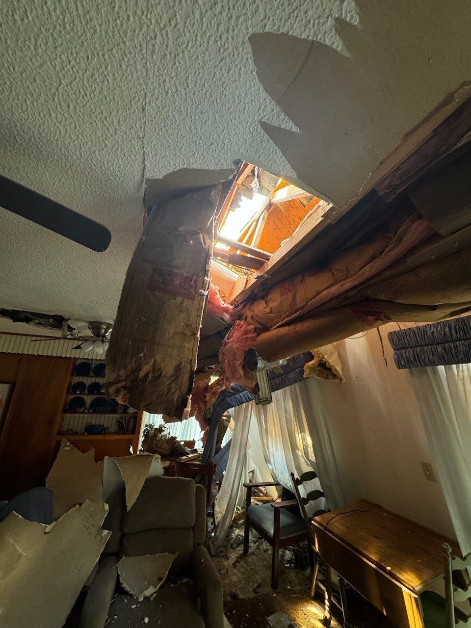 Damaged ceiling with a hole exposing wooden beams, debris scattered. Room appears to be interior.