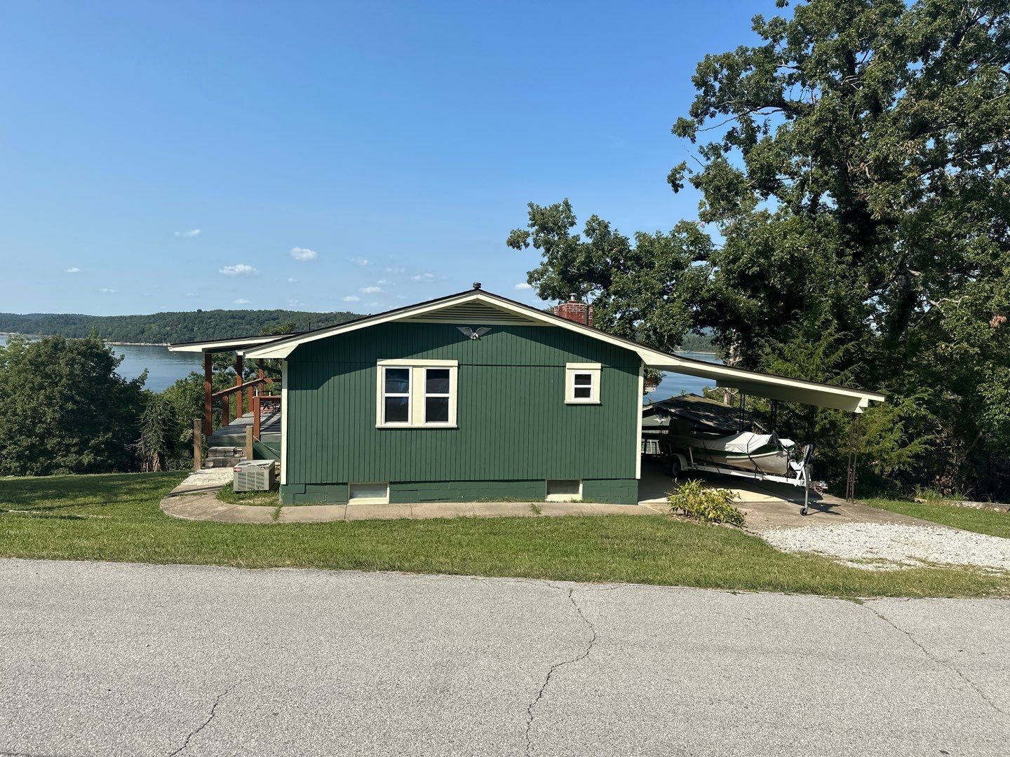 Green cabin with a boat shelter overlooking a lake.