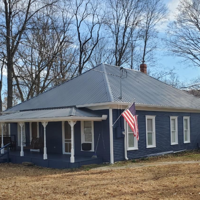 Blue house with metal roof and American flag. Porch with white columns.