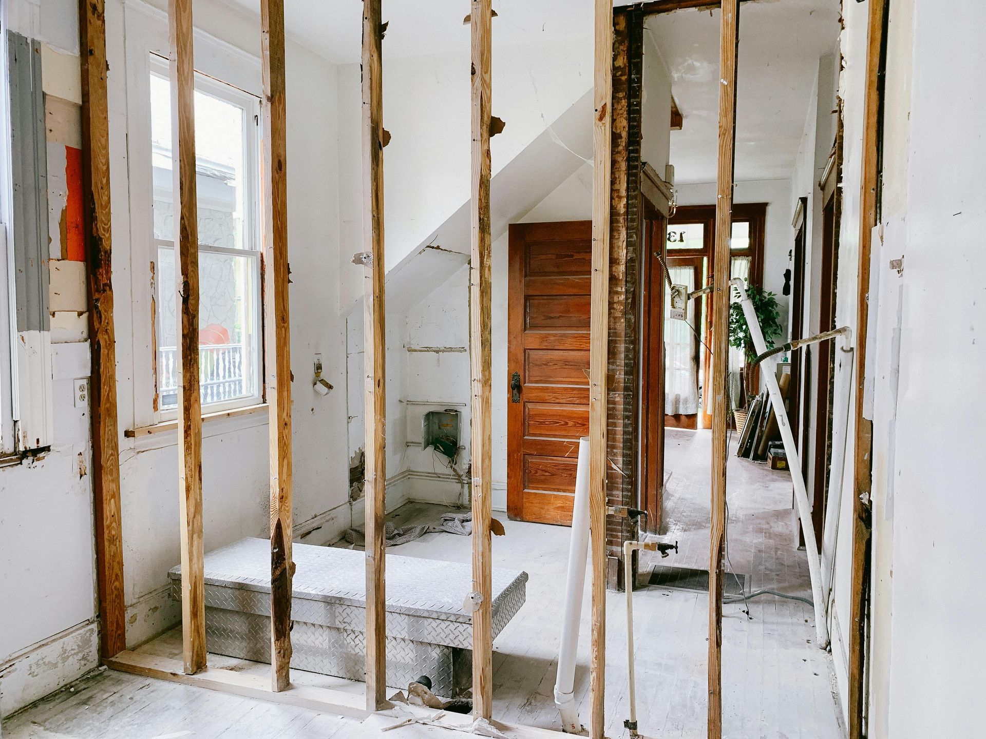 Exposed wall studs in a partially renovated interior hallway with stairs and white walls