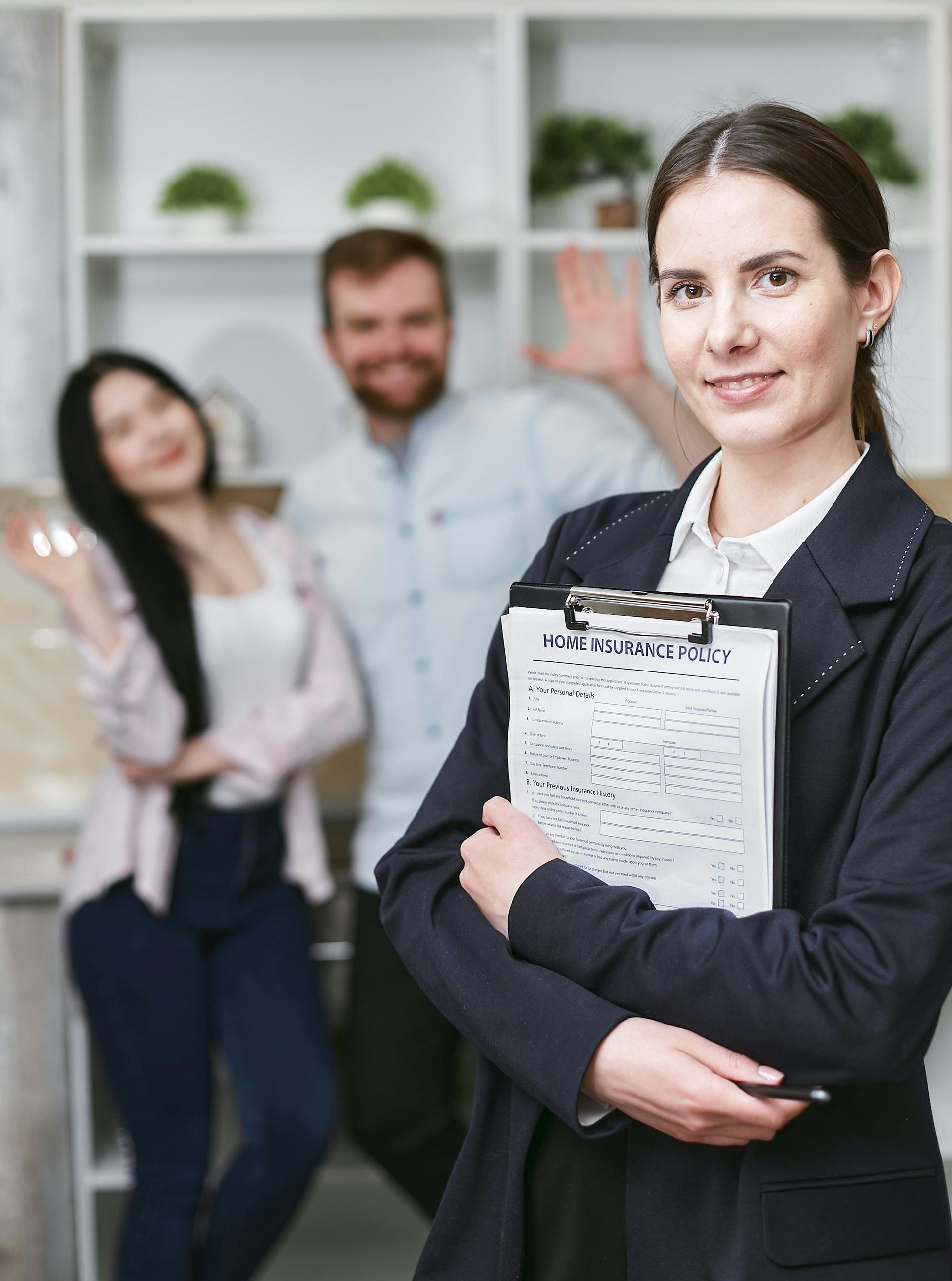 Businesswoman holding a clipboard in an office, with two colleagues blurred in the background.