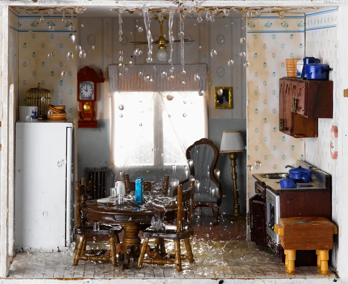 Messy dollhouse kitchen with table, chairs, white fridge, and shelves in a small room