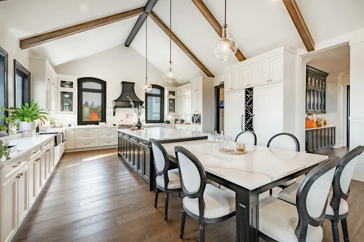 A bright, modern kitchen and dining area with white cabinetry, a kitchen island, hardwood floors, and vaulted ceilings.