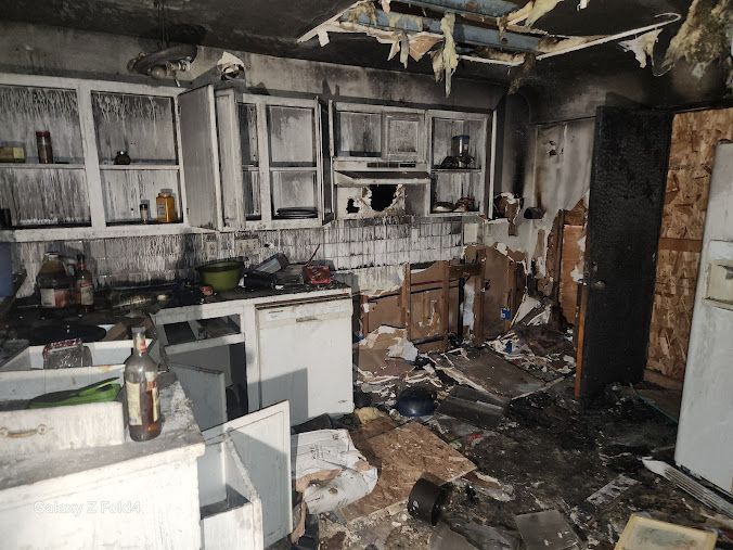 Burned kitchen with charred cabinets, damaged appliances, and debris scattered on the floor