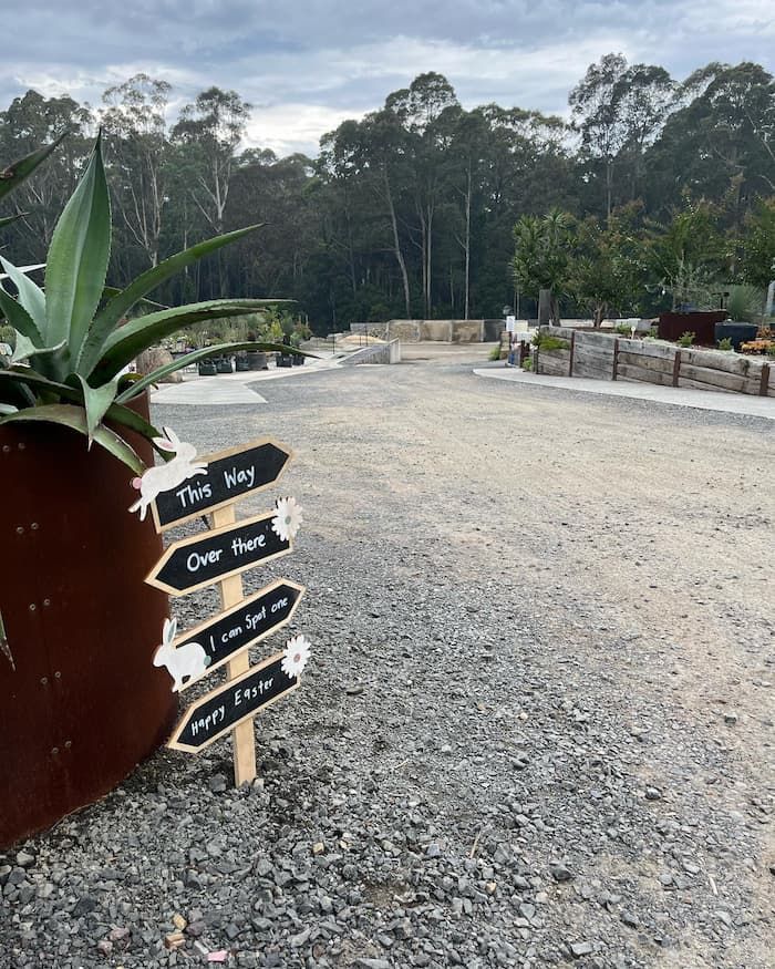 A Potted Plant Is Sitting Next To A Sign On A Gravel Road — Schutz Landscape and Garden Supplies in Jervis Bay, NSW