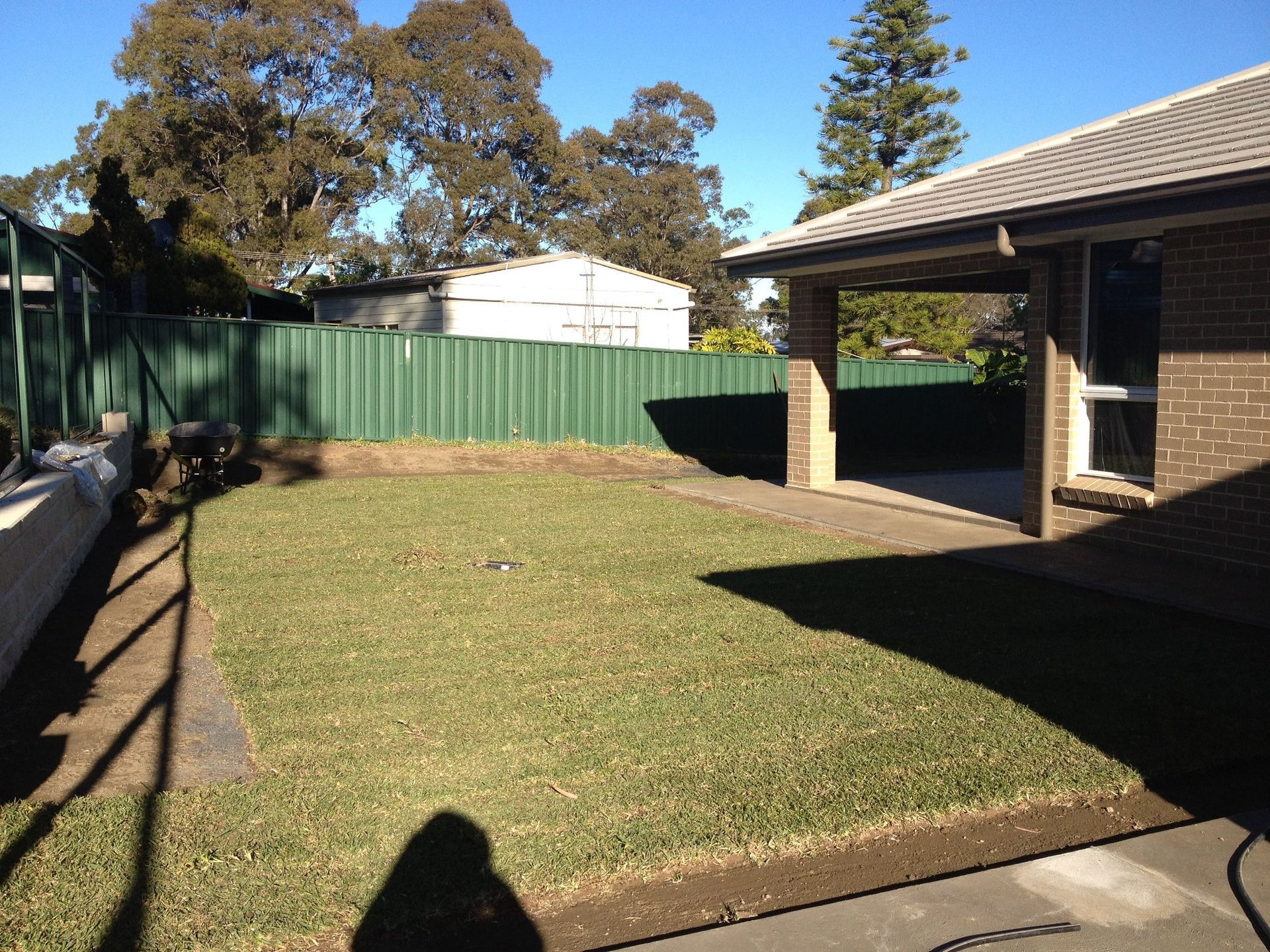 A Brick House With A Green Fence In The Backyard — Schutz Landscape and Garden Supplies in Tomerong, NSW