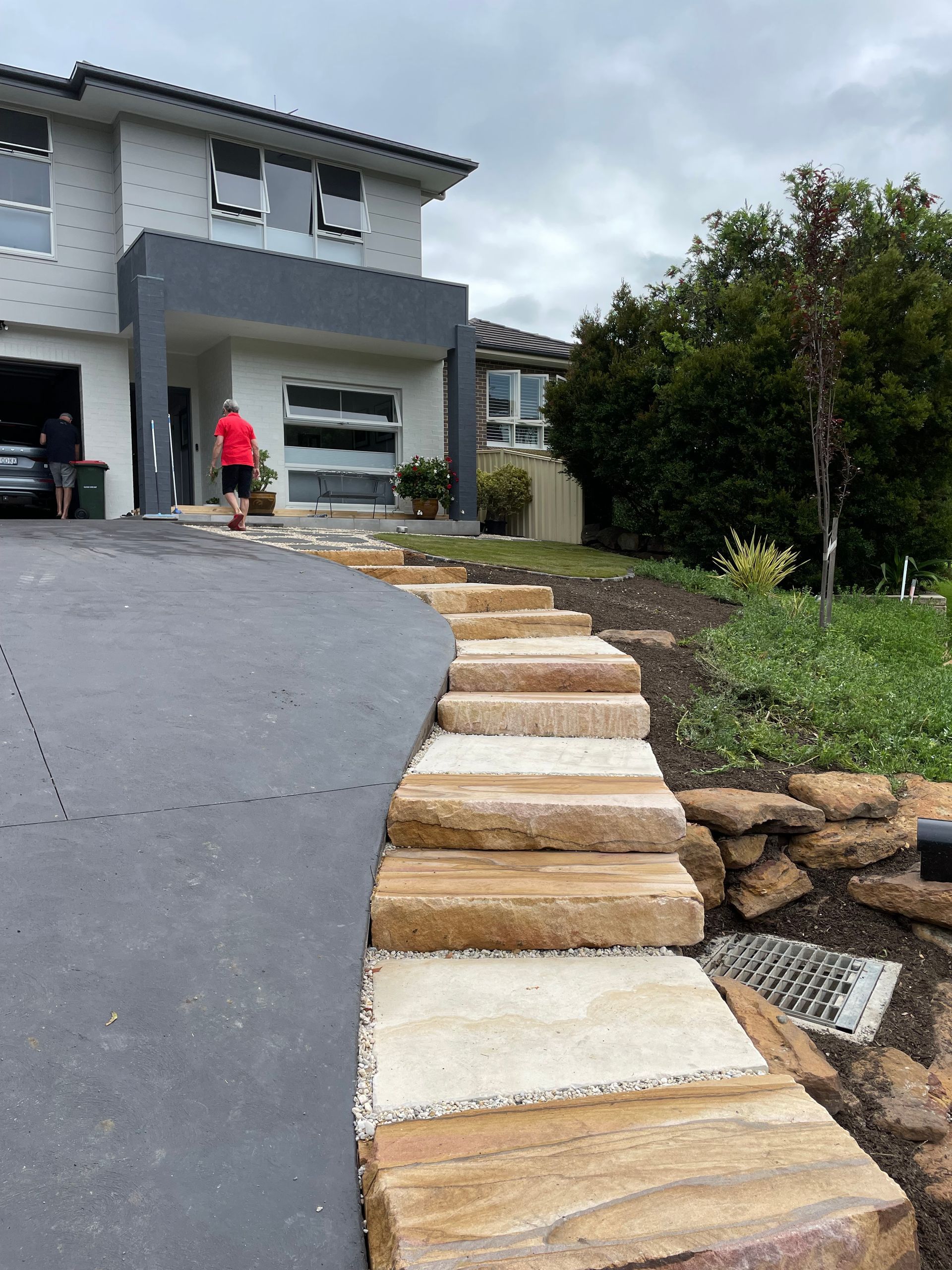 Stone steps lead to a modern home with a dark gray driveway. A person walks up the steps. Overcast day.