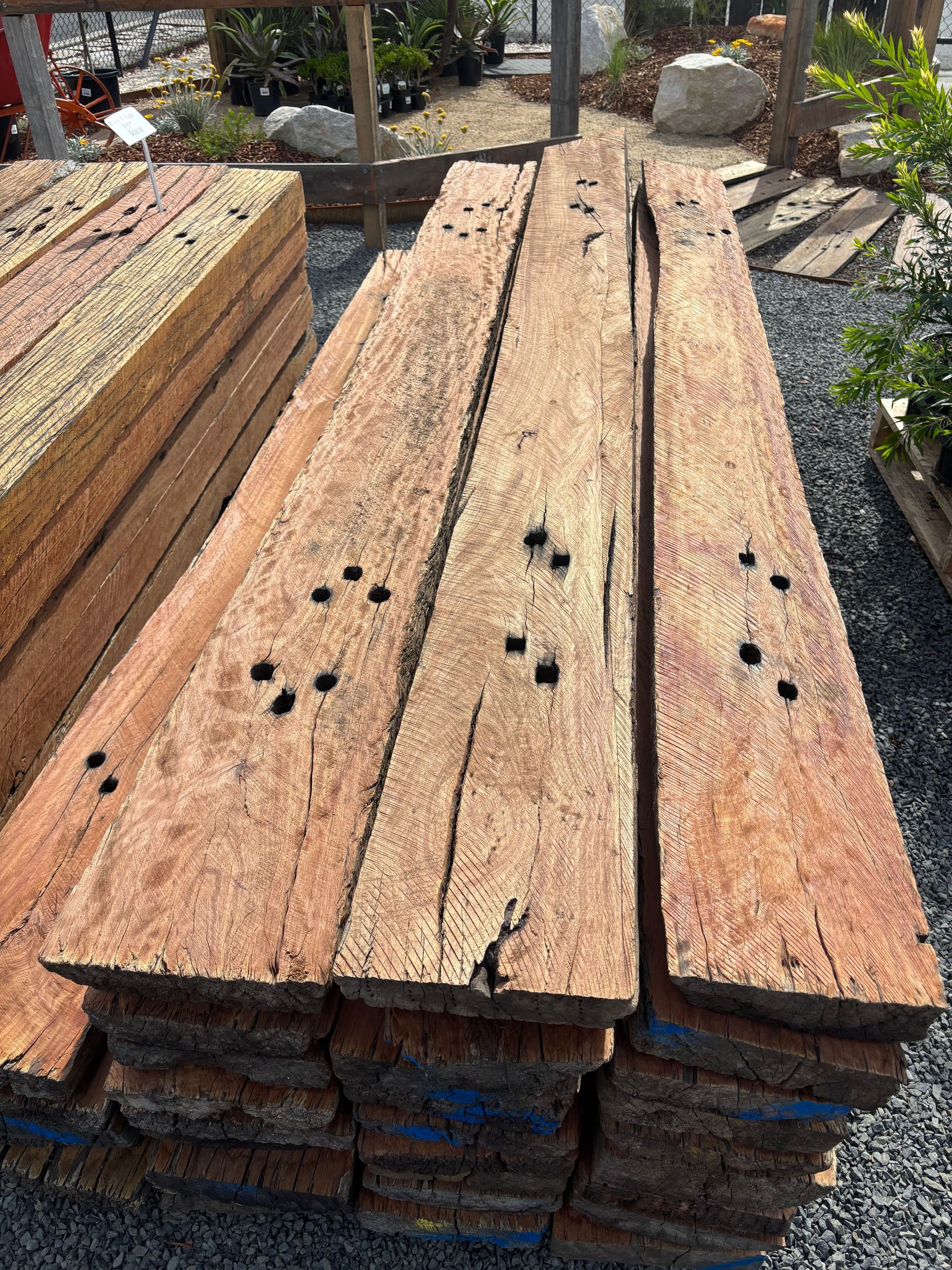 Pile of weathered, brown wooden planks with holes, stacked outdoors — Schutz Landscape and Garden Supplies in Tomerong, NSW
