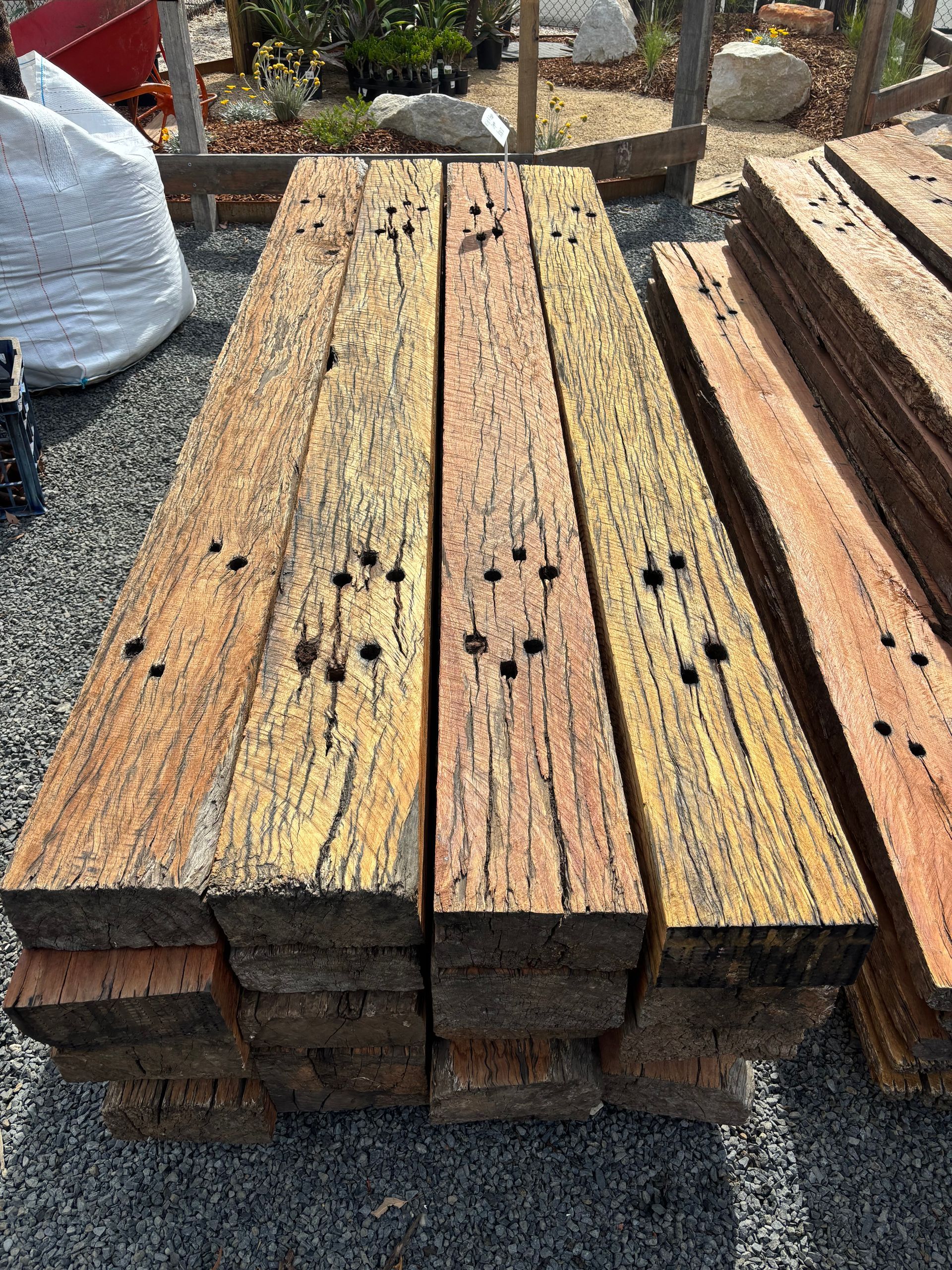 Stack of weathered, rectangular wood beams. Several display bolt holes and varying shades of brown — Schutz Landscape and Garden Supplies in Tomerong, NSW