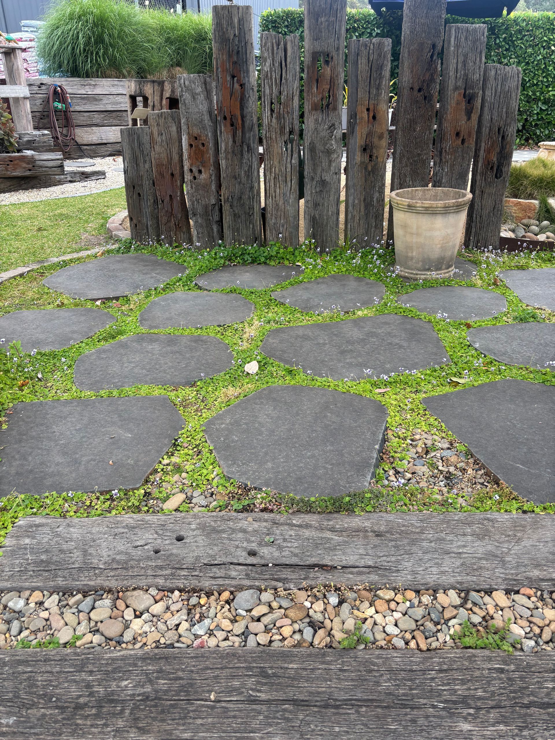 Stone path through grass with wooden posts and a pot in a garden setting — Schutz Landscape and Garden Supplies in Tomerong, NSW