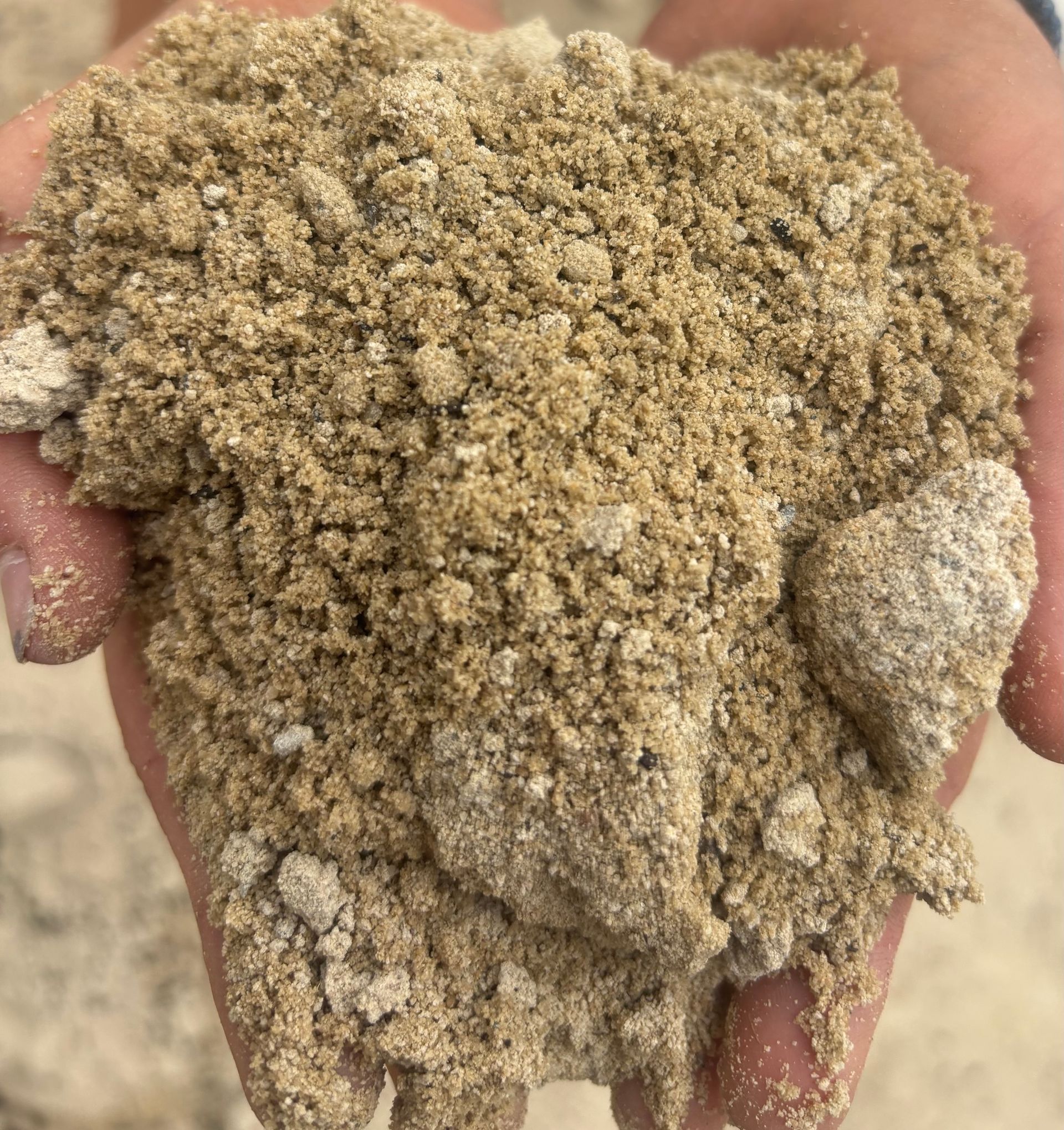 Hands holding a pile of light brown, grainy sand  — Schutz Landscape and Garden Supplies in Tomerong, NSW
