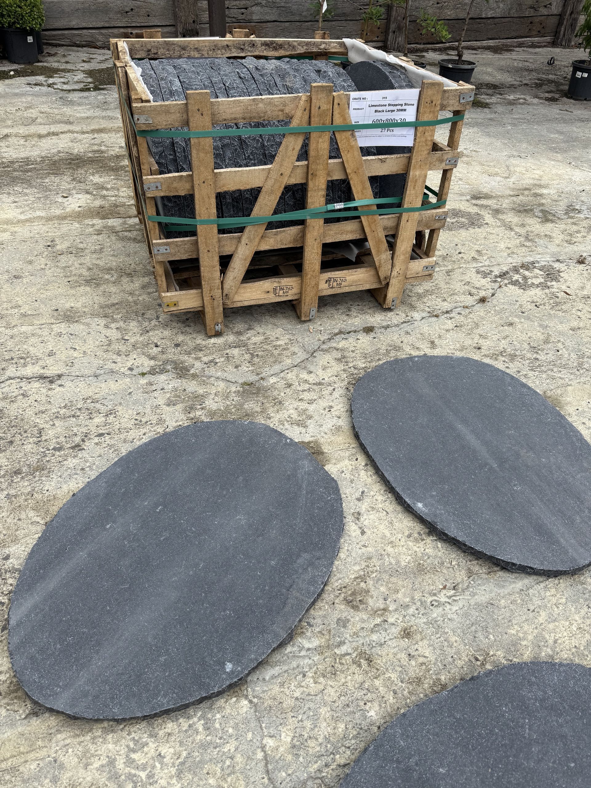 Wooden crate of dark stone tiles, with several oval-shaped tiles in front, on a concrete surface — Schutz Landscape and Garden Supplies in Tomerong, NSW