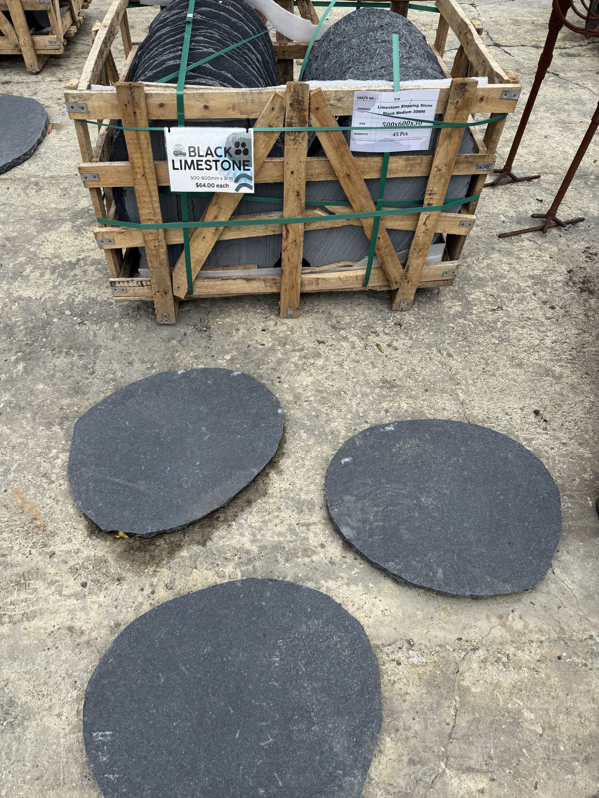 Wooden crate holding black stone pavers, three loose pavers in front on a concrete surface — Schutz Landscape and Garden Supplies in Tomerong, NSW