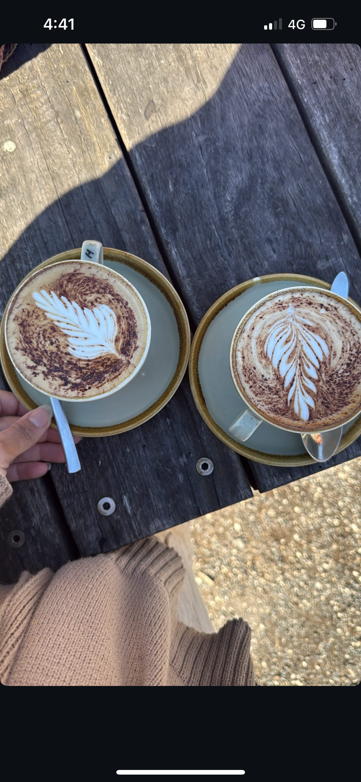 Two lattes with leaf designs on wooden table, sunlight — Schutz Landscape and Garden Supplies in Tomerong, NSW