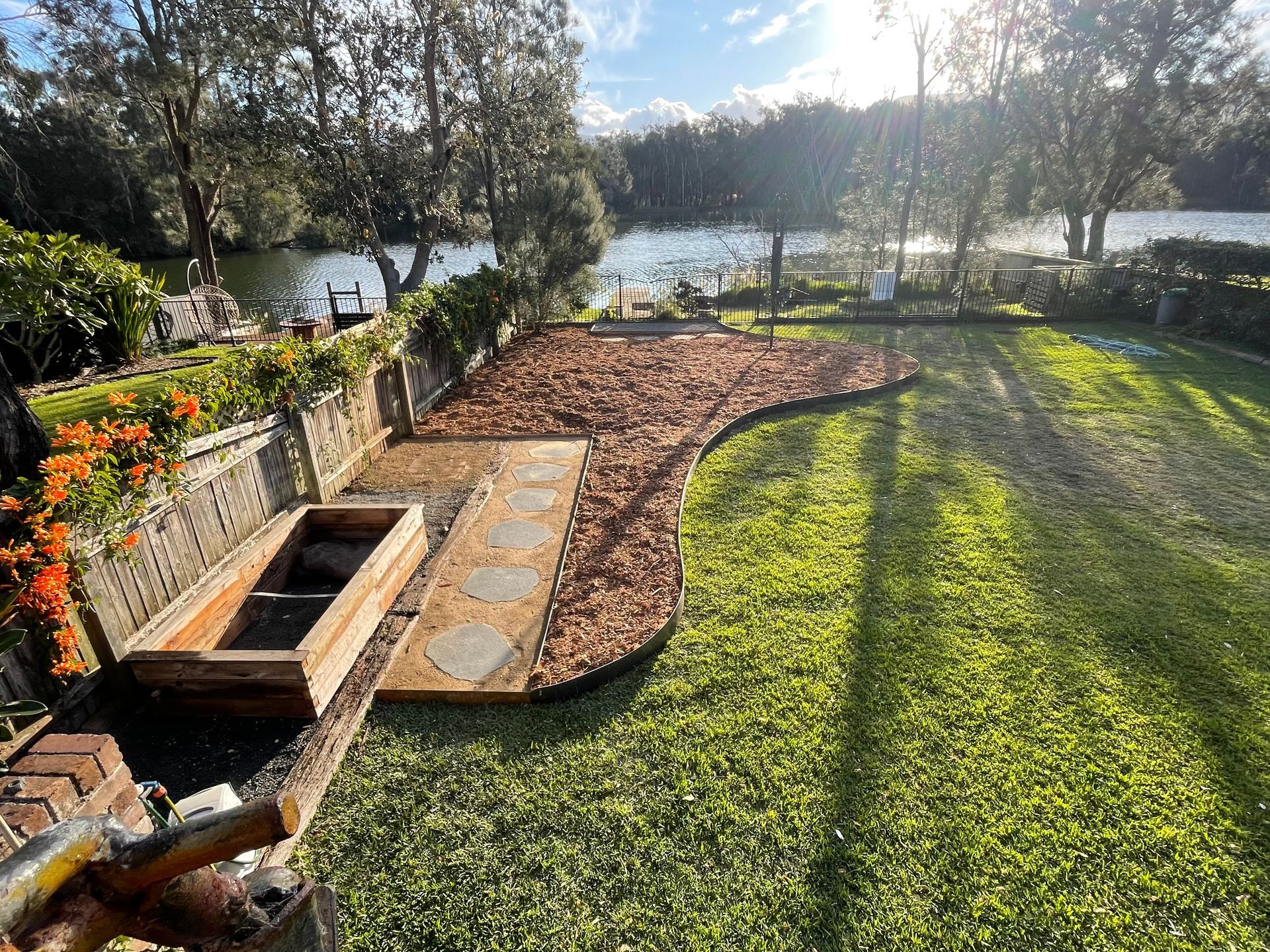 Backyard garden with wood chips, stepping stones, and a view of water and trees.