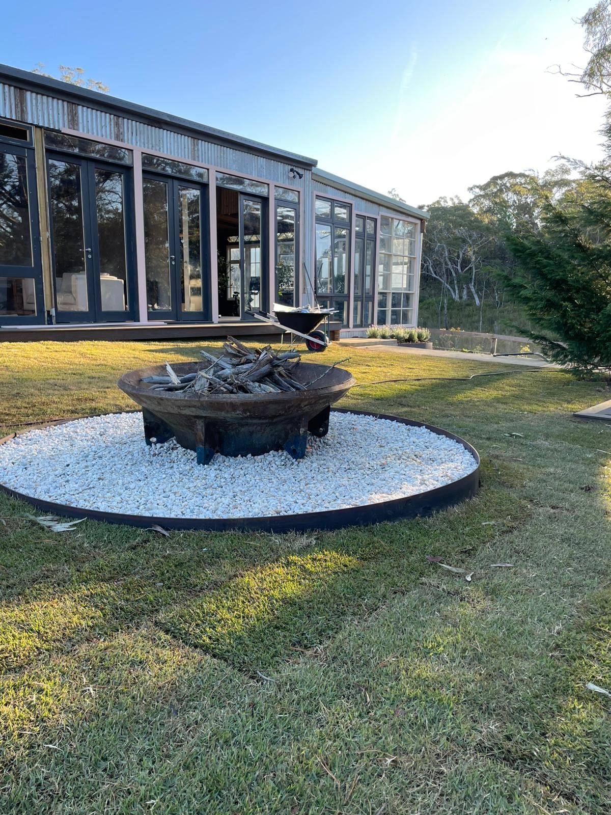 Fire pit surrounded by white stones in a grassy yard, with a modern building in the background.