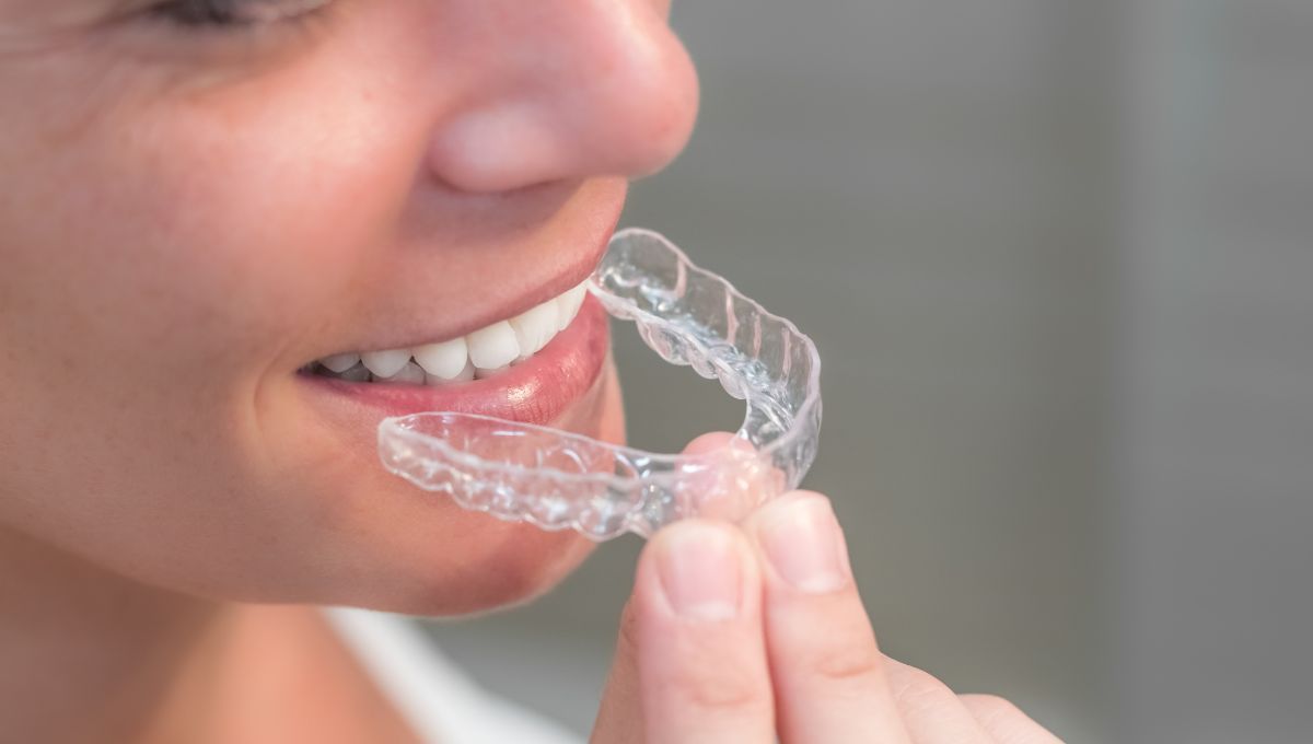 Una mujer sostiene un aparato transparente en su boca.