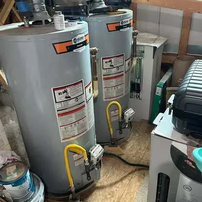 Two gray commercial-style water heaters standing side-by-side in a storage area.